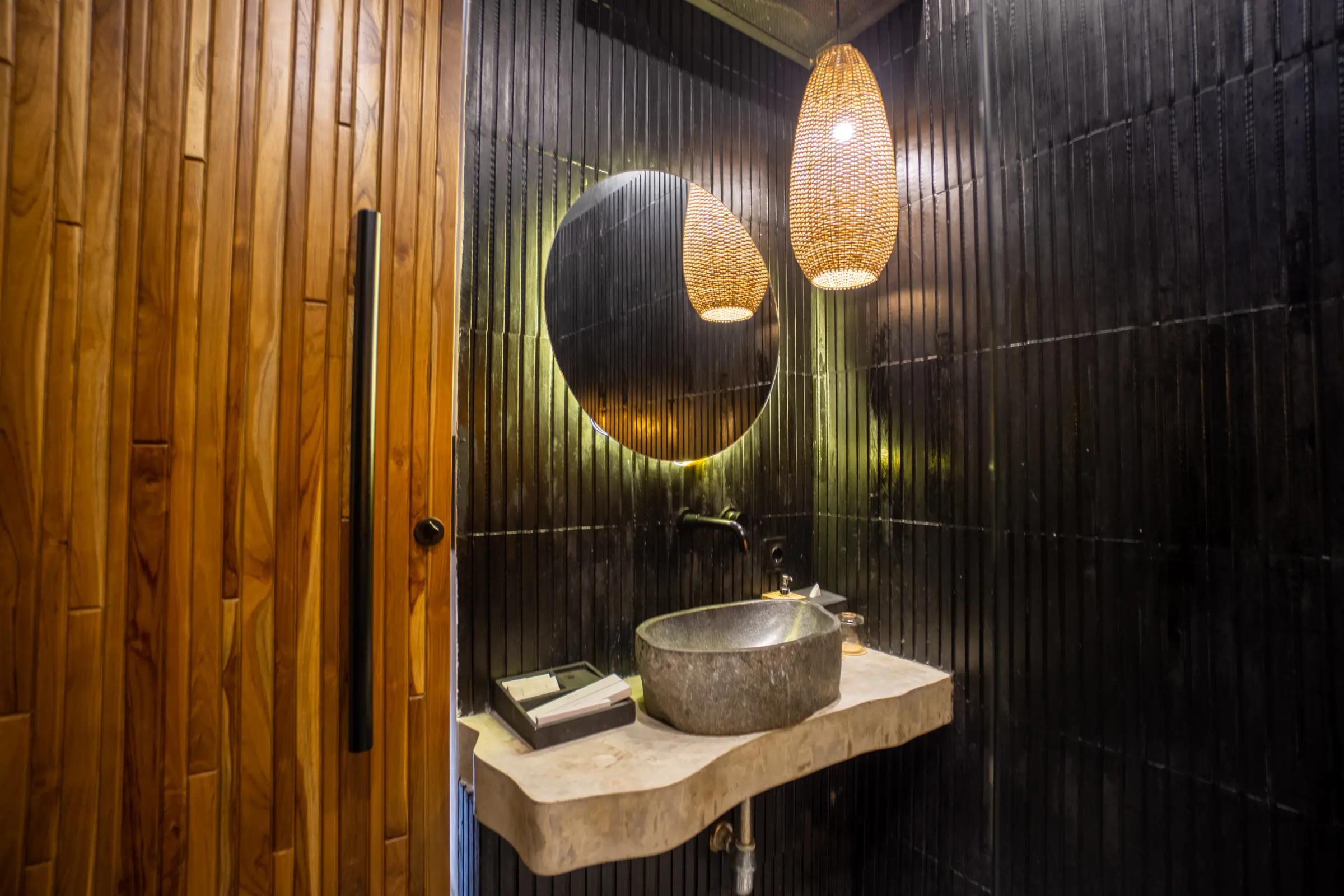 Stone washbasin and round mirror in a bathroom at Rahya Villas, Uluwatu
